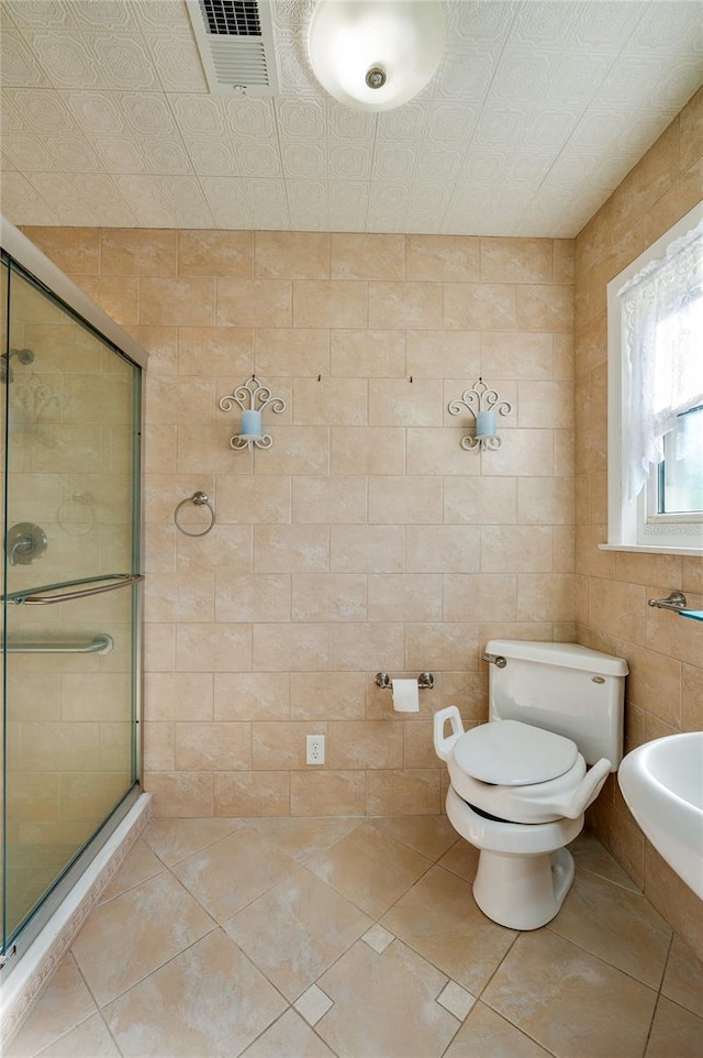 bathroom featuring tile patterned floors, toilet, a shower with door, and tile walls