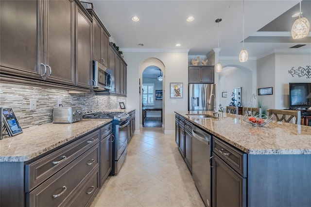 kitchen featuring sink, stainless steel appliances, light stone counters, an island with sink, and decorative light fixtures