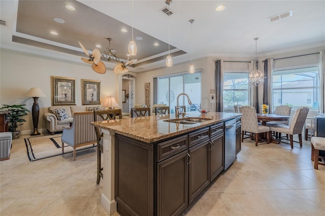 kitchen with light stone counters, hanging light fixtures, a tray ceiling, and an island with sink