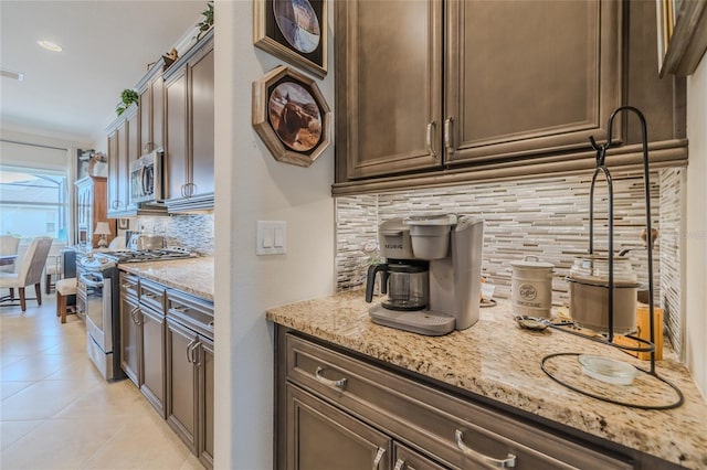 kitchen with stainless steel appliances, dark brown cabinetry, light stone countertops, light tile patterned flooring, and decorative backsplash