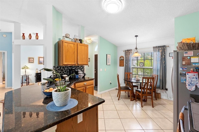 kitchen with stainless steel refrigerator, backsplash, decorative light fixtures, vaulted ceiling, and dark stone counters