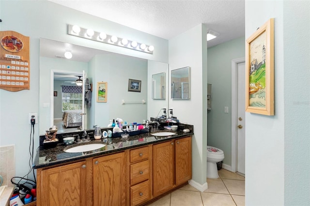 bathroom with ceiling fan, vanity, a textured ceiling, tile patterned floors, and toilet