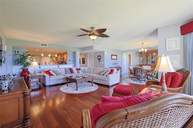 living room featuring ceiling fan with notable chandelier, dark wood-type flooring, and a textured ceiling