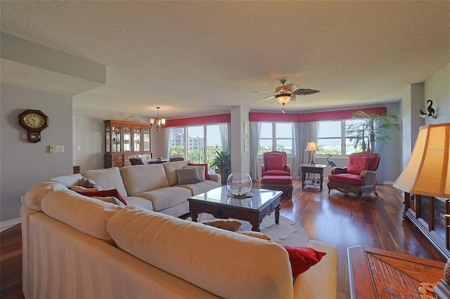 living room featuring dark wood-type flooring, ceiling fan with notable chandelier, and a textured ceiling