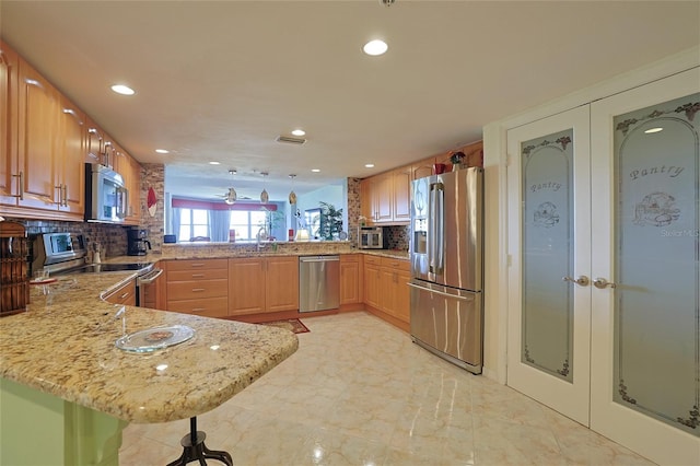 kitchen featuring appliances with stainless steel finishes, a breakfast bar, light stone counters, and kitchen peninsula