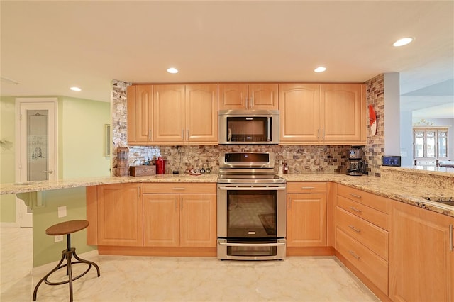 kitchen with light brown cabinetry, light stone counters, kitchen peninsula, and appliances with stainless steel finishes