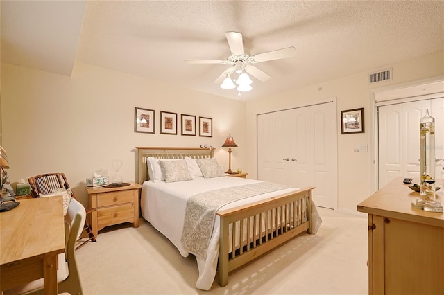 bedroom featuring ceiling fan, multiple closets, light colored carpet, and a textured ceiling