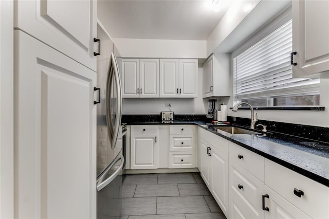 kitchen with a sink, white cabinetry, freestanding refrigerator, and dark stone counters