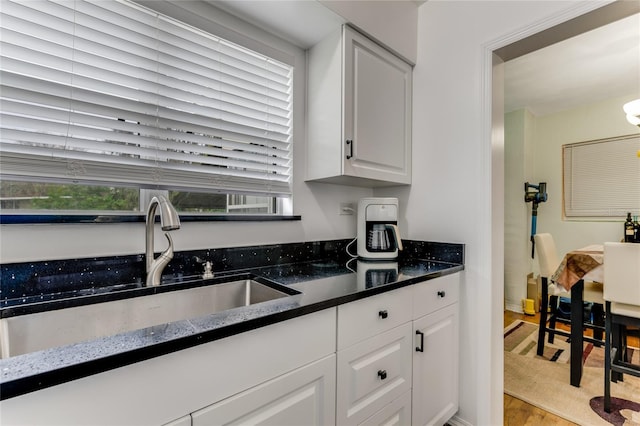 kitchen with white cabinetry, light wood finished floors, dark stone countertops, and a sink