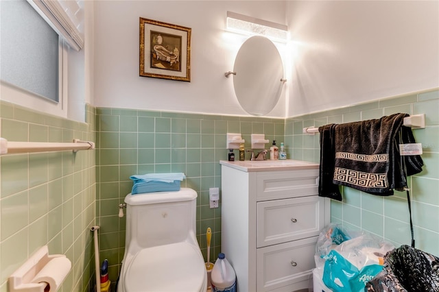 bathroom featuring vanity, toilet, tile walls, and wainscoting