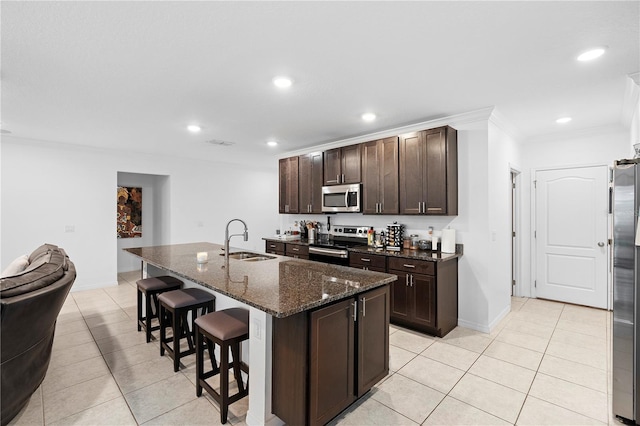 kitchen featuring sink, appliances with stainless steel finishes, dark stone countertops, a kitchen breakfast bar, and a center island with sink