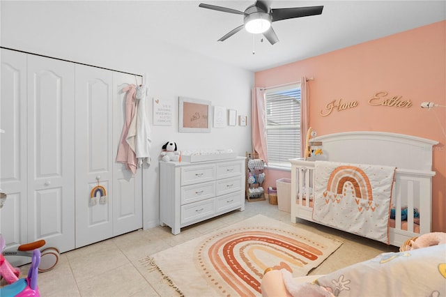 bedroom with light tile patterned flooring, ceiling fan, a closet, and a crib