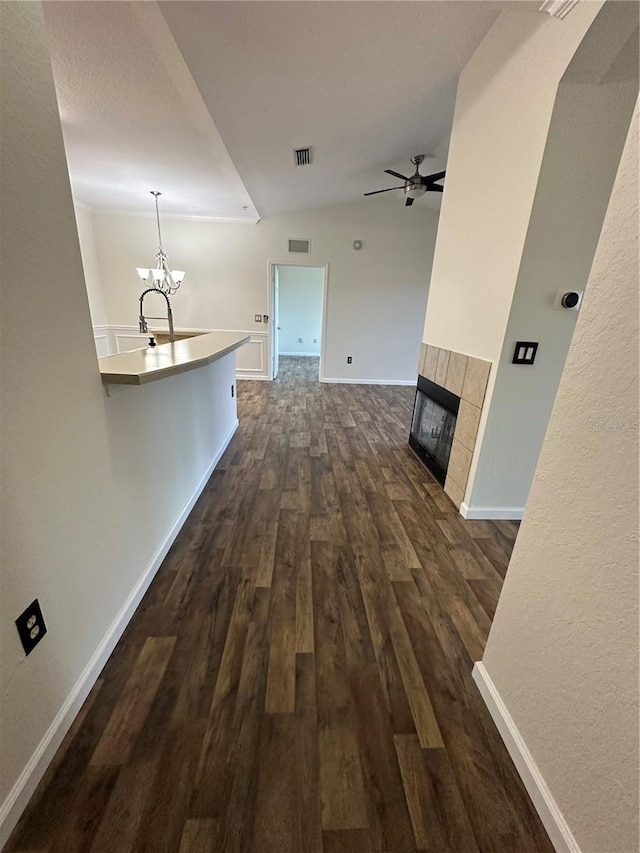 unfurnished living room with sink, dark hardwood / wood-style floors, a tiled fireplace, and ceiling fan with notable chandelier