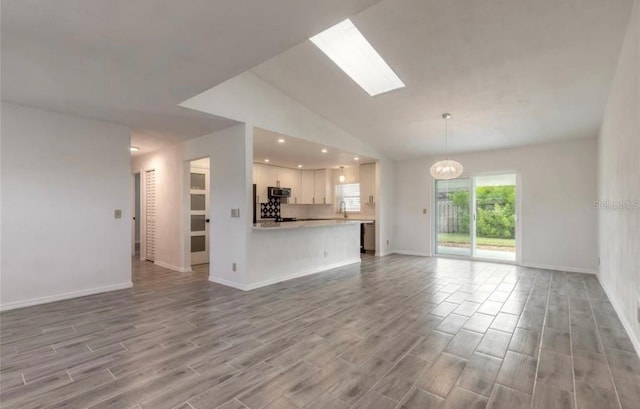 unfurnished living room with an inviting chandelier, sink, light hardwood / wood-style floors, and vaulted ceiling with skylight