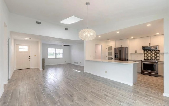 kitchen with appliances with stainless steel finishes, ceiling fan with notable chandelier, decorative light fixtures, white cabinets, and backsplash