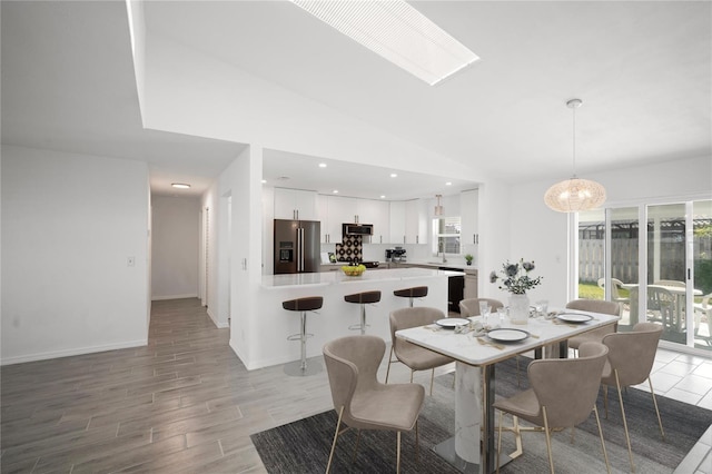 dining space with sink, lofted ceiling with skylight, and light hardwood / wood-style floors