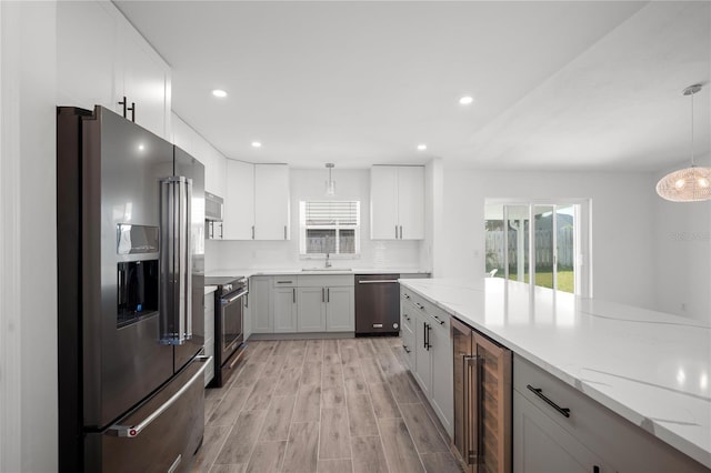 kitchen featuring white cabinetry, decorative light fixtures, appliances with stainless steel finishes, beverage cooler, and light stone countertops