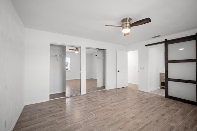 unfurnished bedroom featuring ceiling fan, a barn door, and two closets