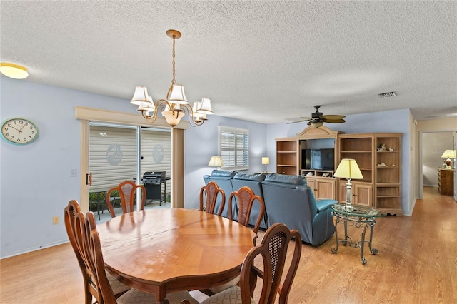 dining space featuring ceiling fan with notable chandelier, a textured ceiling, and light wood-type flooring