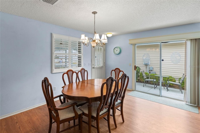 dining area with hardwood / wood-style floors, a textured ceiling, and an inviting chandelier