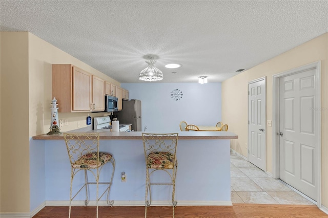 kitchen featuring appliances with stainless steel finishes, light brown cabinets, a kitchen breakfast bar, and kitchen peninsula