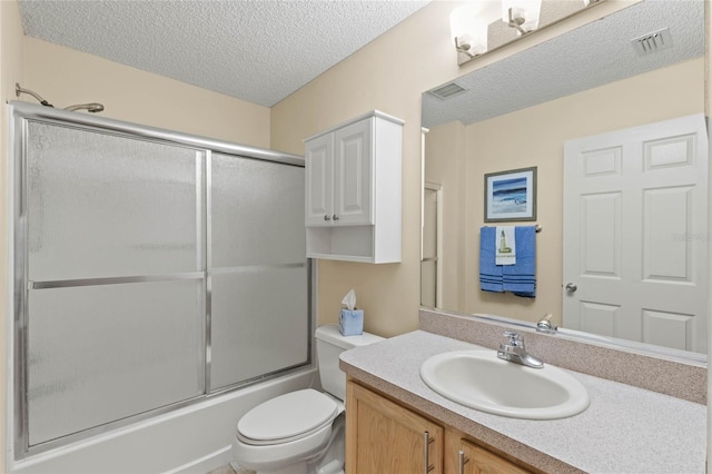 full bathroom with bath / shower combo with glass door, vanity, a textured ceiling, and toilet