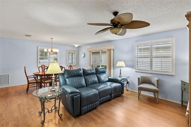 living room featuring ceiling fan with notable chandelier, a textured ceiling, and light wood-type flooring