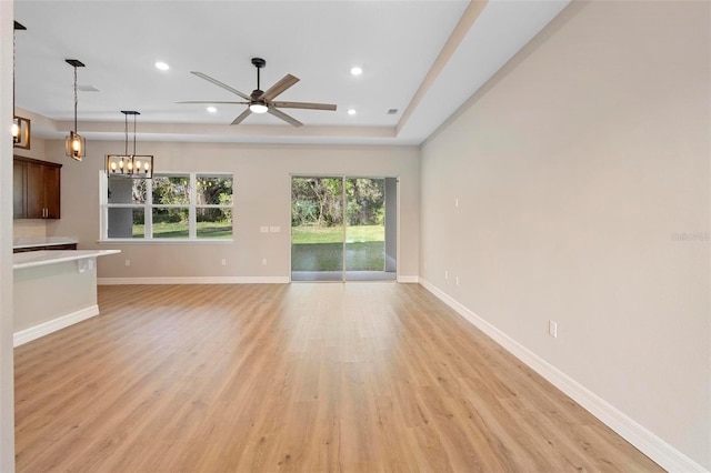 unfurnished living room with a tray ceiling, ceiling fan with notable chandelier, and light hardwood / wood-style floors