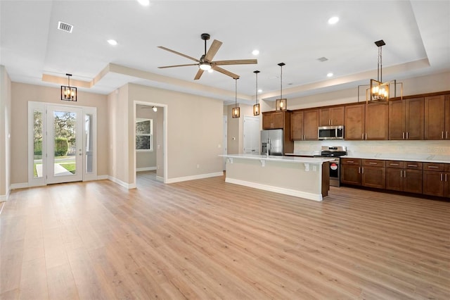 kitchen with stainless steel appliances, a tray ceiling, a kitchen breakfast bar, and an island with sink