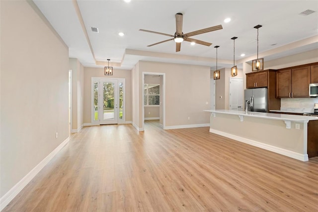 kitchen featuring ceiling fan, hanging light fixtures, stainless steel appliances, a kitchen bar, and light wood-type flooring