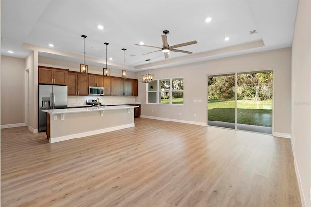 kitchen with a breakfast bar, hanging light fixtures, a center island with sink, a raised ceiling, and stainless steel appliances