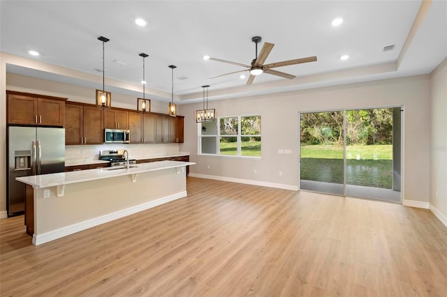 kitchen with appliances with stainless steel finishes, a tray ceiling, a kitchen breakfast bar, and a center island with sink