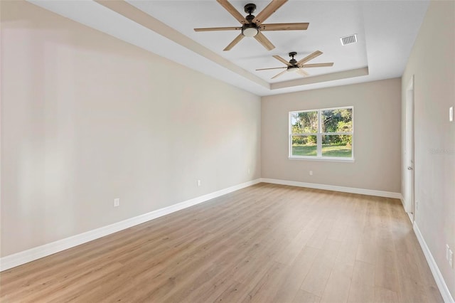 empty room featuring a raised ceiling and light hardwood / wood-style flooring