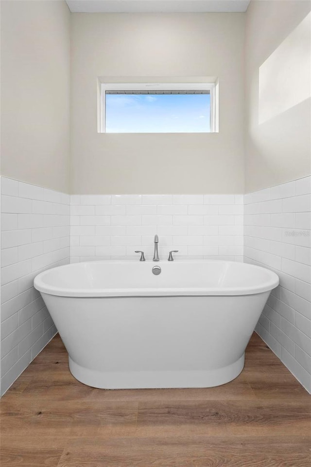 bathroom featuring a tub to relax in, a healthy amount of sunlight, wood-type flooring, and tile walls