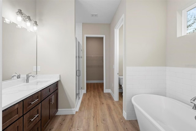 full bathroom featuring hardwood / wood-style flooring, tile walls, separate shower and tub, vanity, and toilet