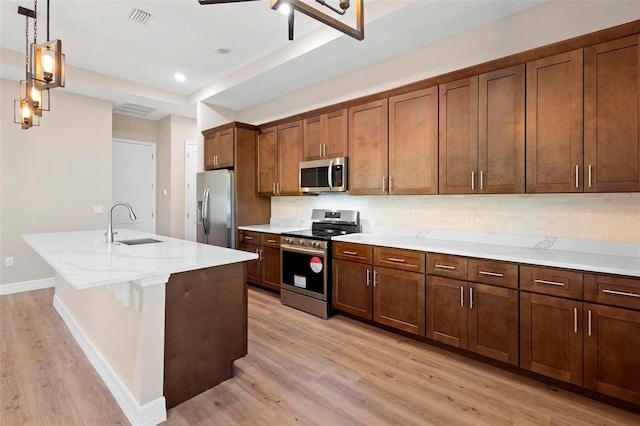 kitchen with pendant lighting, a breakfast bar, appliances with stainless steel finishes, a center island with sink, and light wood-type flooring