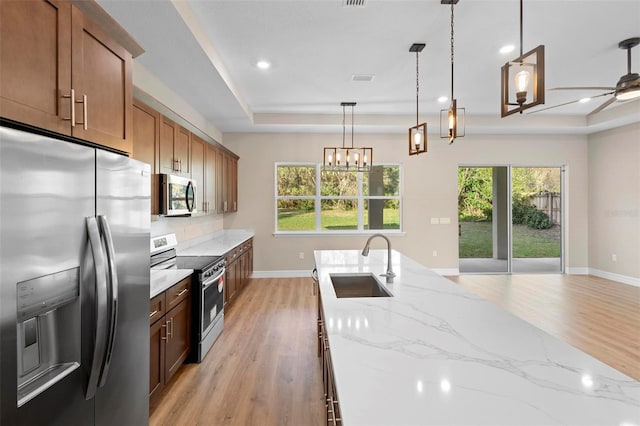 kitchen featuring sink, hanging light fixtures, stainless steel appliances, light stone counters, and a tray ceiling