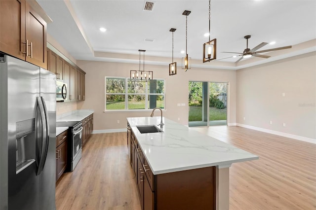 kitchen featuring sink, appliances with stainless steel finishes, decorative light fixtures, a raised ceiling, and light wood-type flooring