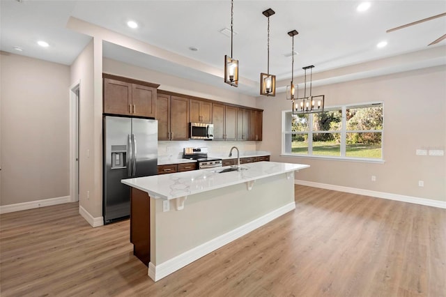 kitchen with sink, a kitchen island with sink, stainless steel appliances, a kitchen bar, and decorative light fixtures