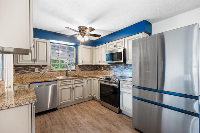 kitchen with sink, backsplash, stainless steel appliances, light hardwood / wood-style floors, and light stone countertops