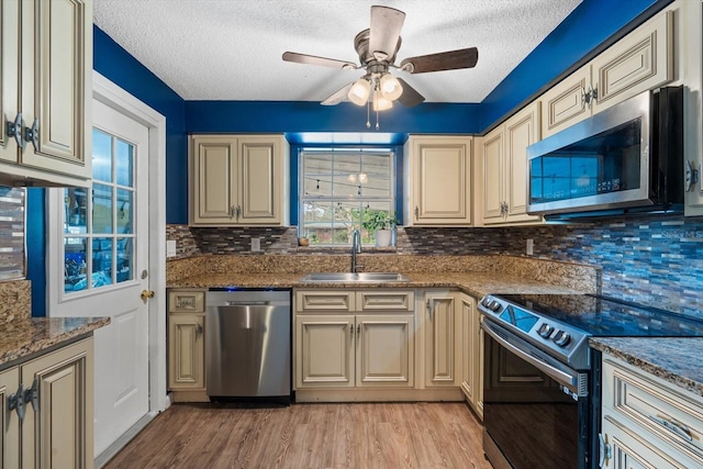 kitchen featuring appliances with stainless steel finishes, sink, dark stone countertops, light hardwood / wood-style floors, and cream cabinets