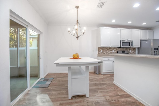 kitchen with pendant lighting, stainless steel appliances, light hardwood / wood-style floors, decorative backsplash, and white cabinets