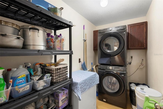 laundry room with light hardwood / wood-style flooring, cabinets, a textured ceiling, and stacked washing maching and dryer