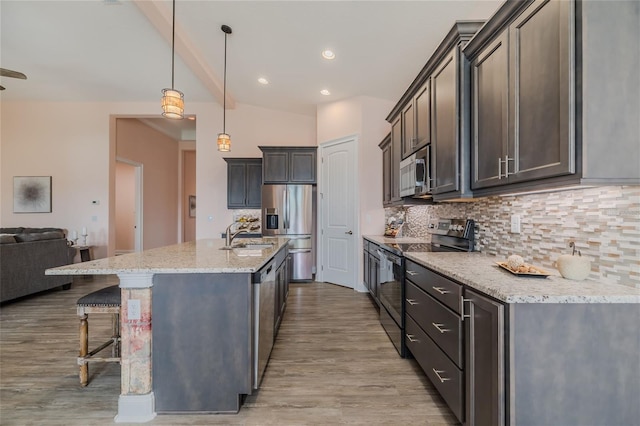 kitchen featuring a kitchen island with sink, light stone countertops, tasteful backsplash, appliances with stainless steel finishes, and pendant lighting