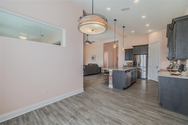 kitchen with a center island with sink, ceiling fan, stainless steel appliances, hanging light fixtures, and a breakfast bar area