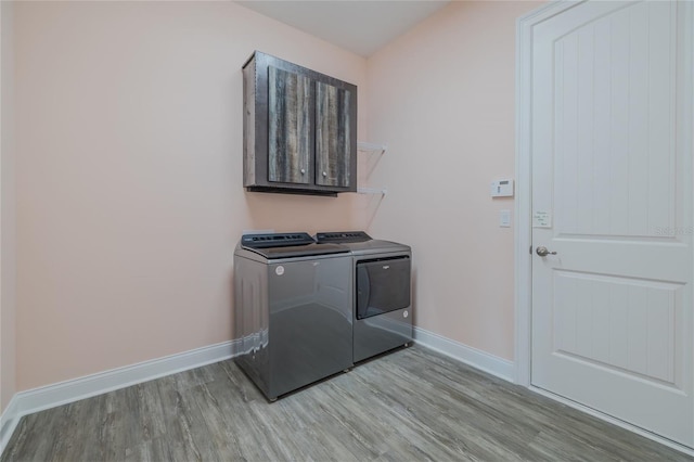 clothes washing area featuring washing machine and dryer, light wood-type flooring, and cabinets