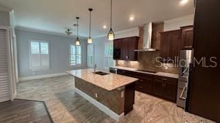 kitchen featuring wall chimney exhaust hood, sink, hanging light fixtures, a kitchen breakfast bar, and an island with sink