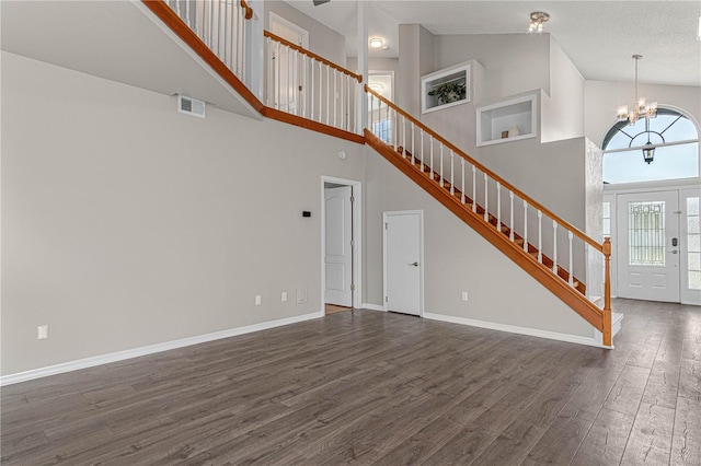 unfurnished living room featuring visible vents, an inviting chandelier, dark wood-type flooring, baseboards, and stairs