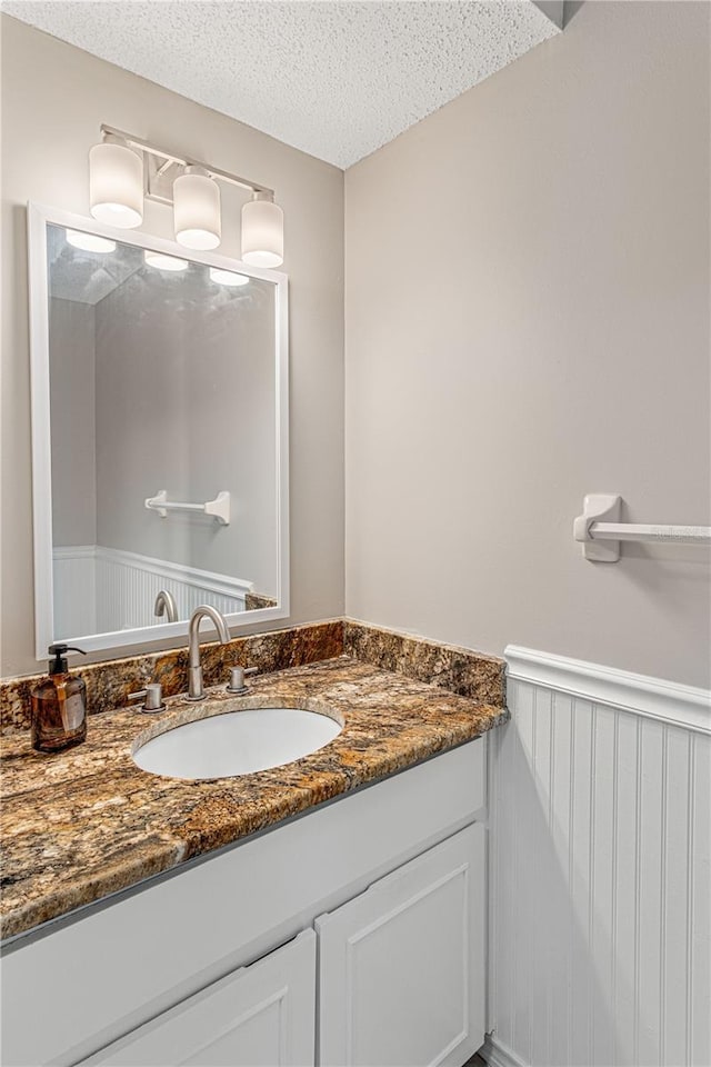 half bath with vanity, a textured ceiling, and wainscoting