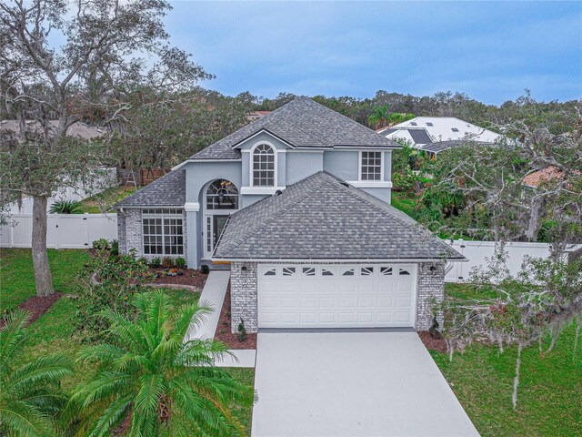 traditional-style home featuring a garage, fence, driveway, and a shingled roof